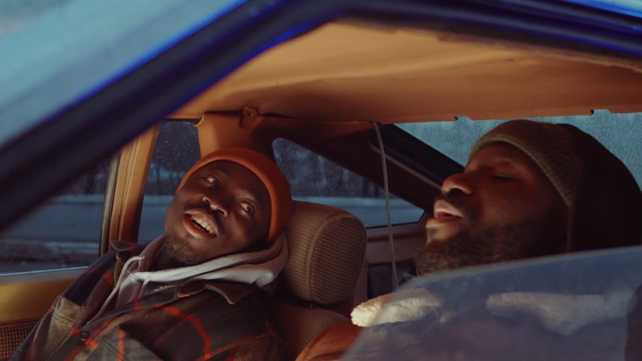 두 명의 흑인 남자가 차에 앉아서 저녁에 이야기하고 있습니다.