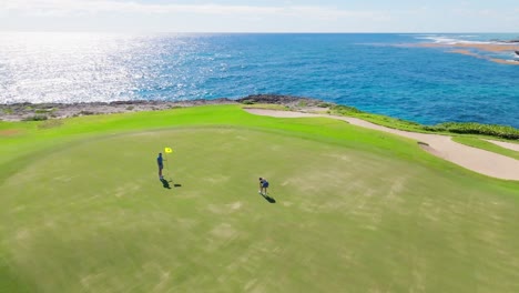 Drone-flying-around-couple-playing-golf-on-Corales-Golf-Course-with-sea-in-background,-Punta-Cana-Resort-in-Dominican-Republic