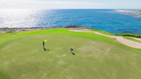 drone flying around couple playing golf on corales golf course with sea in background, punta cana resort in dominican republic