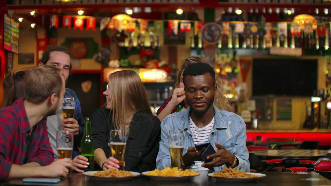 A large group of friends in the bar sitting at the table laughing and chatting drinking beer.