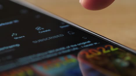 primer plano de un dedo tocando el botón de suscripción de un teléfono móvil en una aplicación de redes sociales.