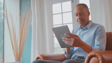 mature man at home sitting in armchair streaming movie to digital tablet