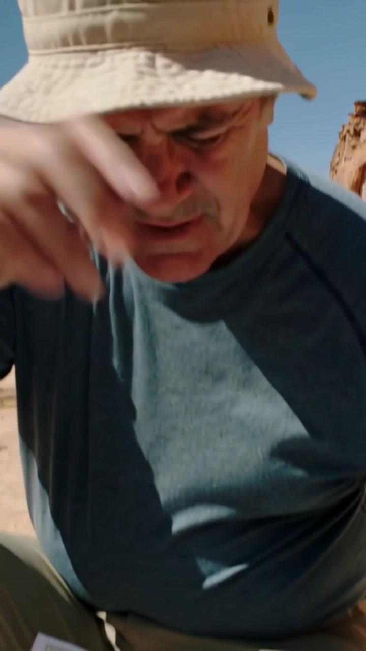 Vertical video: Pausing hiker scanning map on rock, in bucket hat, coughing while navigating route