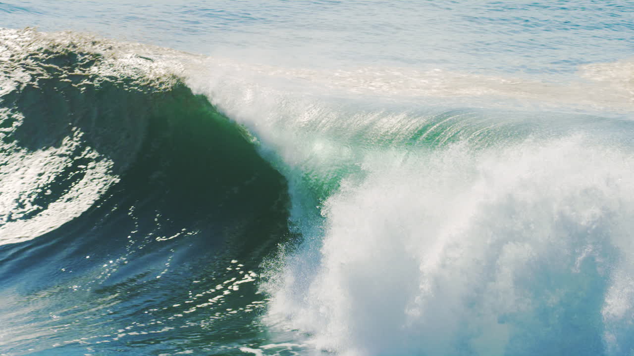 Slow motion view of surfer sitting on boards as stunning green wave barrels and crashes across open ocean waters