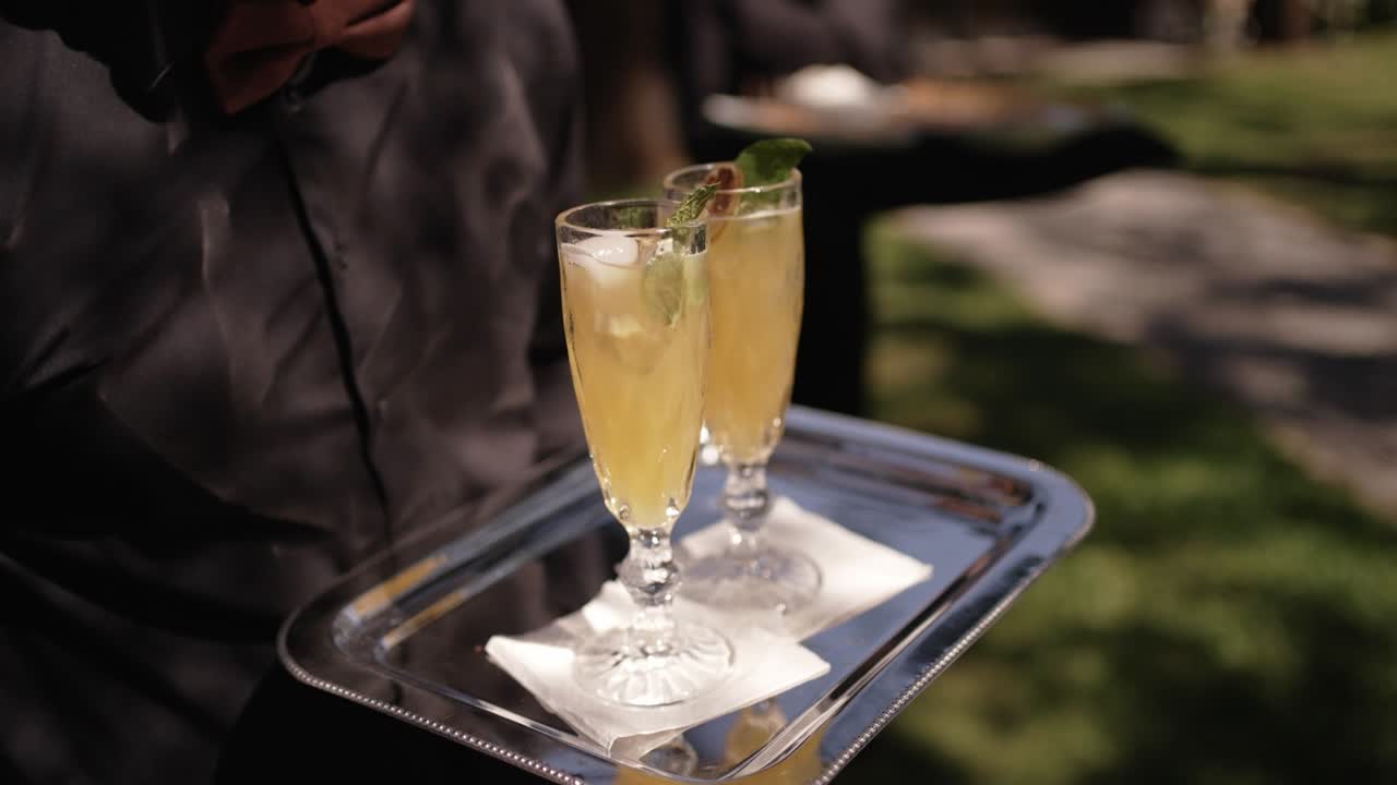Waiter carries a silver tray with two elegant cocktails garnished with mint outdoors