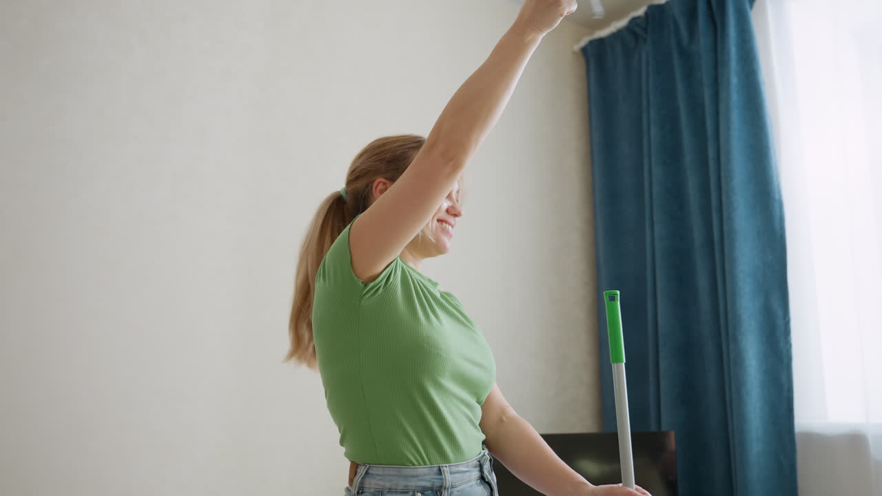 Una donna chic fa roteare allegramente il mocio mentre un adolescente pulisce la struttura del letto, unendo pulizia e divertimento, lavoro di squadra, stile di vita positivo e atmosfera domestica vivace, sottolineando la responsabilità domestica