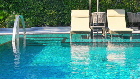 two deckchairs under umbrella poolside at a tropical resort with lush background