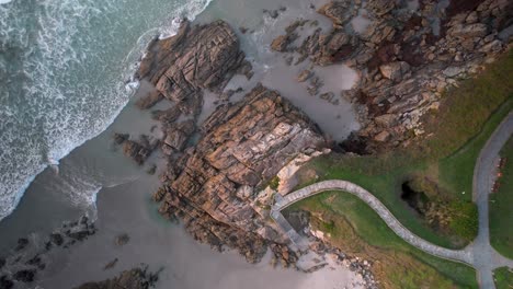 Overhead-View-Of-Rocky-Coastline,-Waves,-And-Path-To-The-Beach-In-Caion,-A-Coruña,-Spain