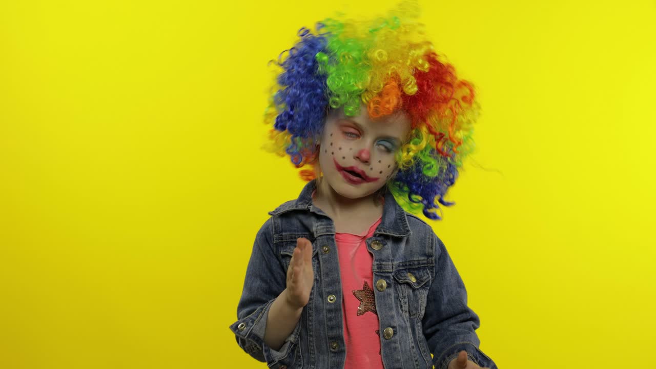 niña payaso en peluca haciendo caras tontas. divirtiéndose, muestra los movimientos del mimo. halloween
