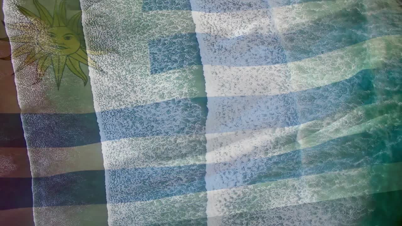animación de la bandera de uruguay ondeando sobre vista aérea de las olas en el mar