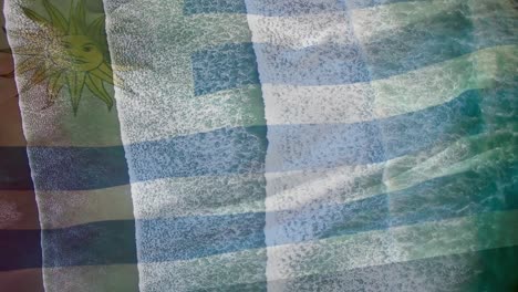 animation of flag of uruguay waving over aerial view of waves in sea