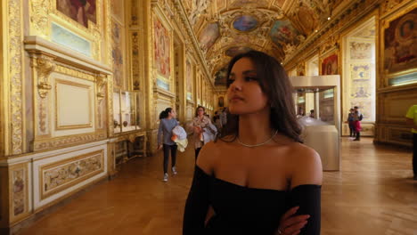 Beautiful-elegant-young-woman,-walking-in-a-gold-decorated-corridor,-in-the-Louvre-Museum,-Paris,-France