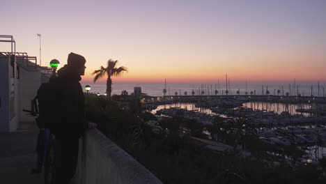 Sightseeing-silhouette-man-takes-photo-of-harbor-bay-during-golden-sunset-sky