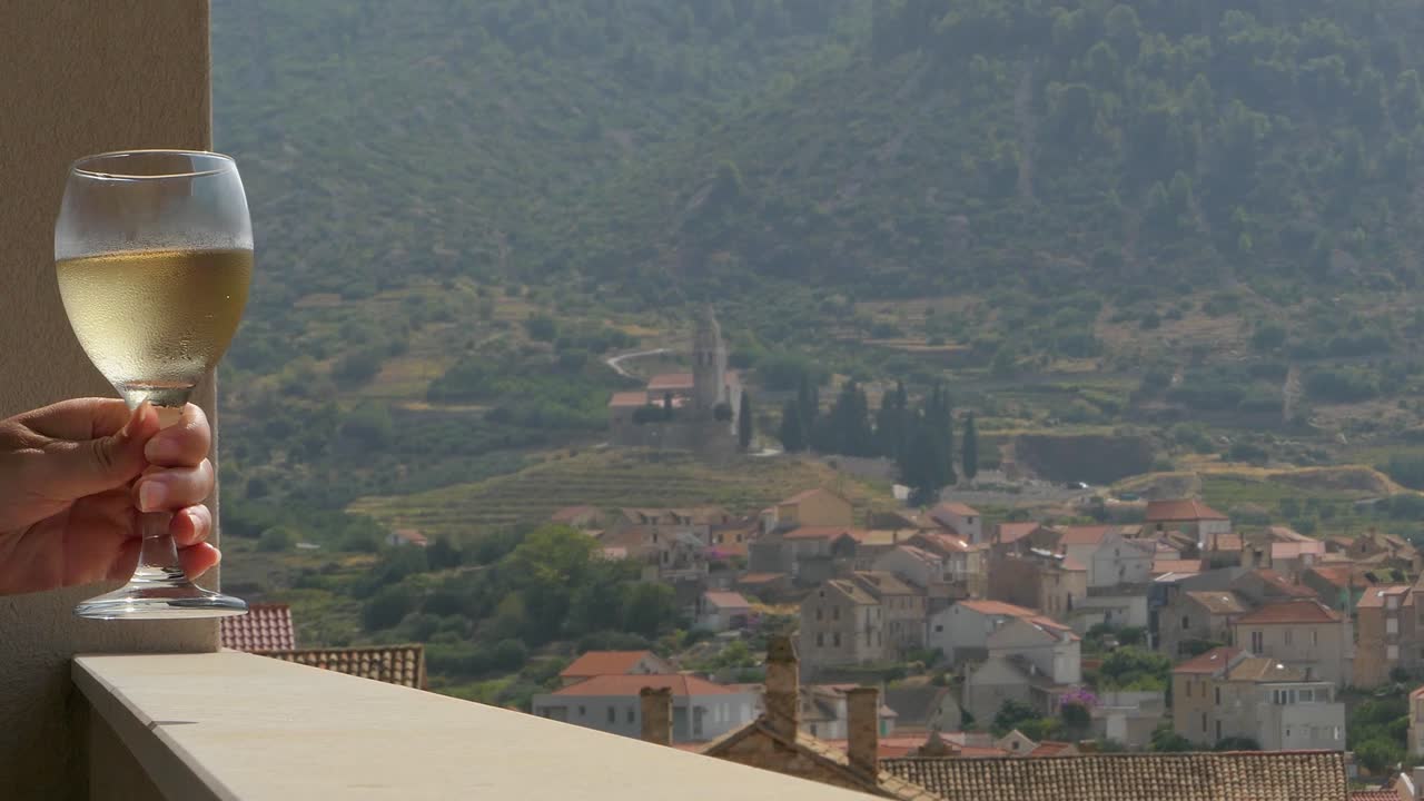 Tenere un bicchiere di vino su un balcone, vista montagne e centro storico, Komiza, Vis, Croazia