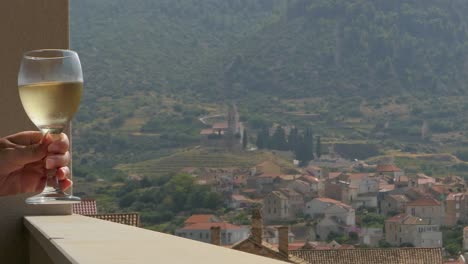 Holding-wine-glass-on-balcony,-mountains-and-old-town-view,-Komiza,-Vis,-Croatia