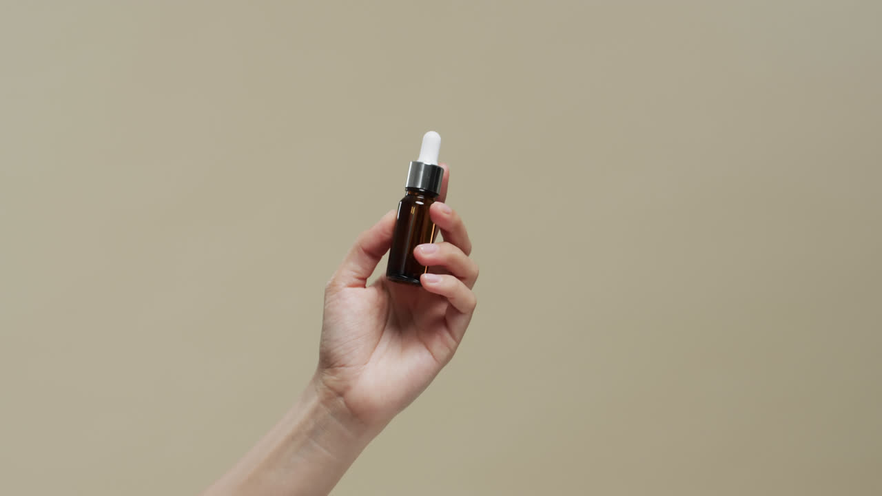 mano de mujer sosteniendo un frasco con cosméticos en fondo beige con espacio de copia, cámara lenta