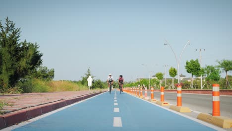 smiling friends cycling on cycle path at sunny summer day, talking and laughing. cyclists riding bicycles on bicycle lane, relaxing and enjoying sunshine, having fun outdoors. healthy lifestyle