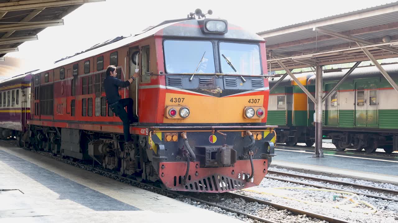 Railway conductor climbs onto stationary vintage diesel locomotive at bright outdoor Bangkok train platform