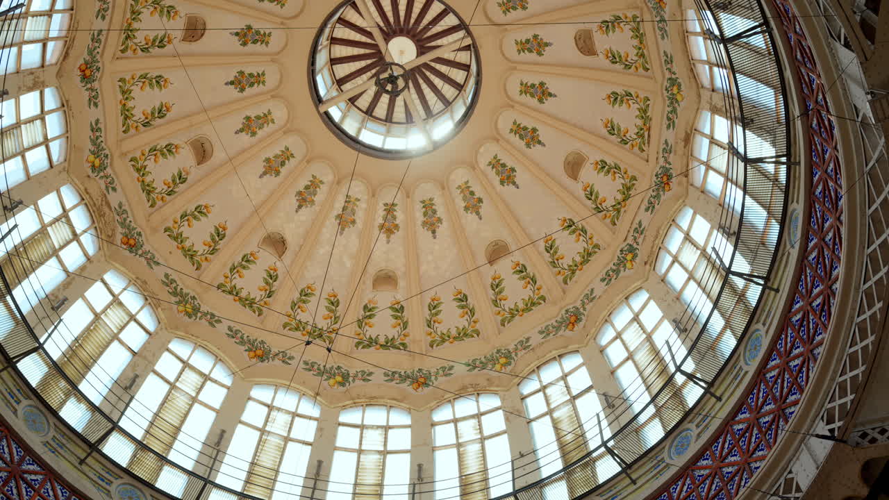 Upward view of a round dome painted with citrus motifs, light streaming through tall window in a church in Valencia, Spain