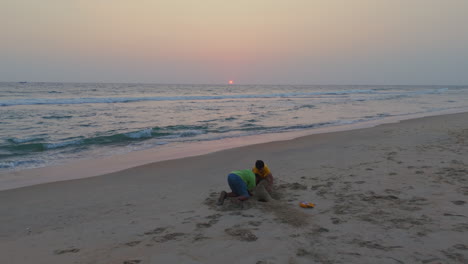 hermanos jugando en la playa, niños jugando con arena al atardecer