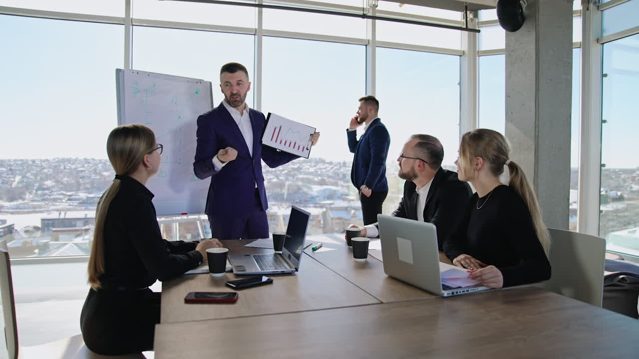 Young team of colleagues having communication at business meeting and discussing chart. Man talking on the phone near the window at backdrop.