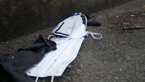 dirty discarded used corona virus masks and gloves waste on street blowing in wind with copy space