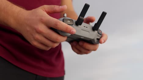 Man holding drone controller outdoors, wearing a red shirt with sky in the background