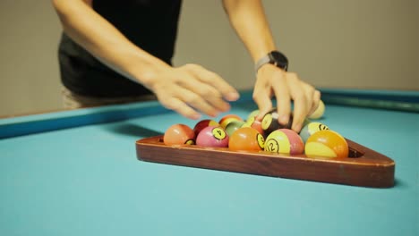 close-up shot of young male person preparing billiard balls in a triangle rack before pool game