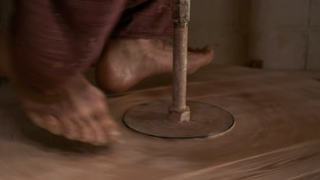 the potter rotates the wooden wheel of the potter's wheel with his feet