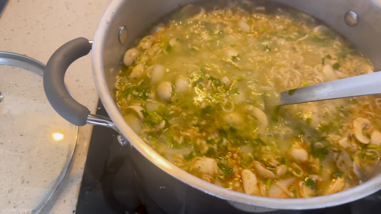 Una persona solleva un coperchio e mescola una zuppa tailandese di pesce e frutti di mare bollente con noodles e funghi
