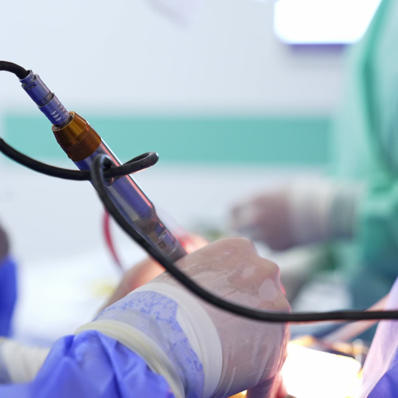 Electric metal device with wire in the gloved hands of a surgeon. Close up. Nurse at backdrop using the syringe. Blurred background