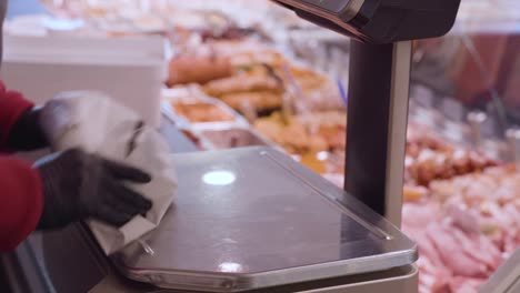 un trabajador de delicatessen uniformado y enguantado pesa y envuelve un paquete de carne fresca según lo ordenado