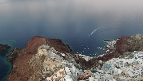 drone view in greece flying over santorini with oia town white houses and blue roofs on a cliff next to the mediterranean sea at sunrise