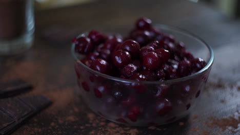 Man-hand-put-glass-bowl-with-frozen-cherries-on-wooden-table