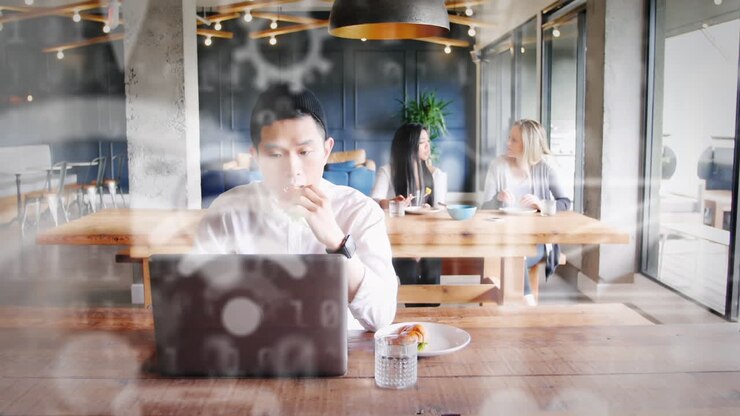 Icone digitali sullo sfondo di un uomo che usa il portatile mentre fa colazione.