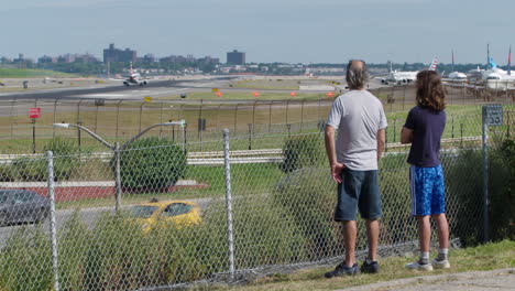 father and son watch plane land at laguardia airport from park overlooking grand central parkway