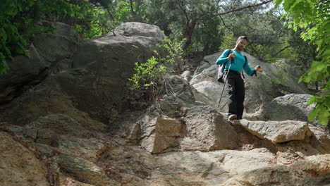 Low-Angle-View-Man-Hiker-Walking-Downhill-Rocky-Mountain-Forest-Trail-with-Trekking-Poles-while-Hiking-in-Wild-Nature-on-Summer-Day