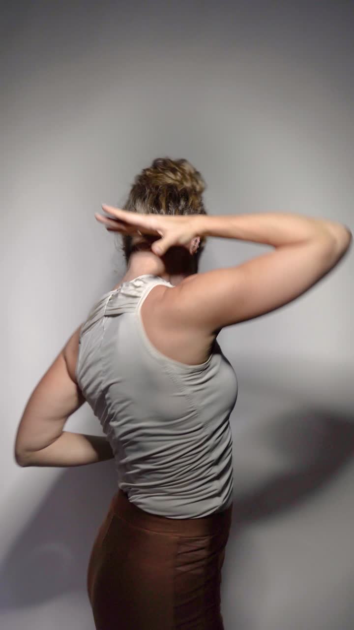 A skilled female dancer gracefully performs expressive movements with elegance and artistry, set on a simple gray background
