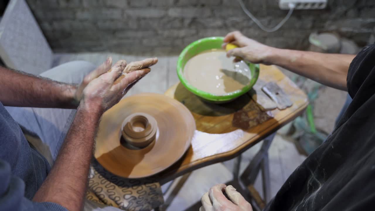 dos personas trabajando en la rueda de cerámica