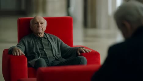 elderly man sitting in red chair in museum