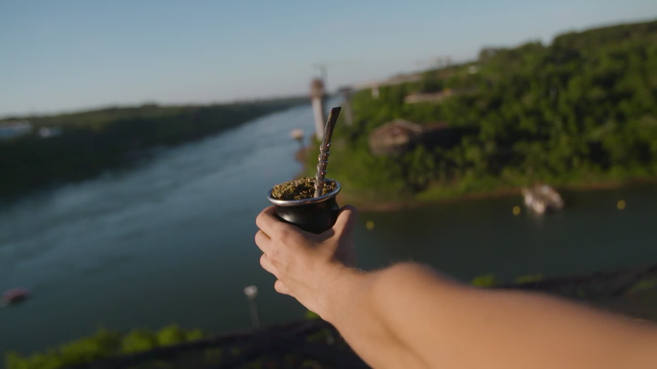 Hand holding traditional Argentine mate overlooking the Iguazu river landscape