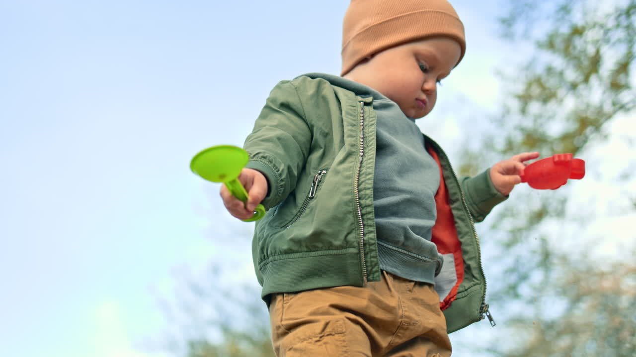 Little two-year-old boy plays with sand outside in a sandbox. Toddler boy digs sand with a shovel on a playground. Child's walk outdoors