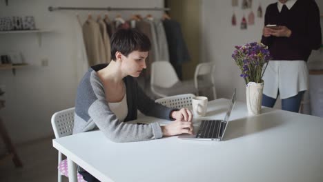 Mujer-Joven-Sentada-En-La-Mesa-Y-Escribiendo-En-La-Computadora-Portátil.-Mujer-Usando-Teléfono-Inteligente