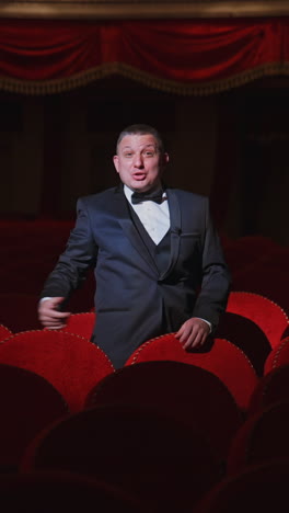 man in empty theater. rich man in suit taking off facial mask and says something among rows of red seats in the theater without audience. world crisis at pandemic. vertical video