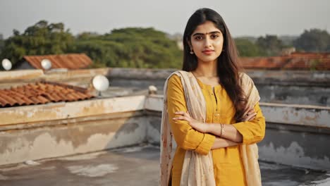 young indian woman in traditional yellow clothing standing confidently on a rooftop, embodying pride in her cultural heritage against a blurred backdrop of rooftops and trees