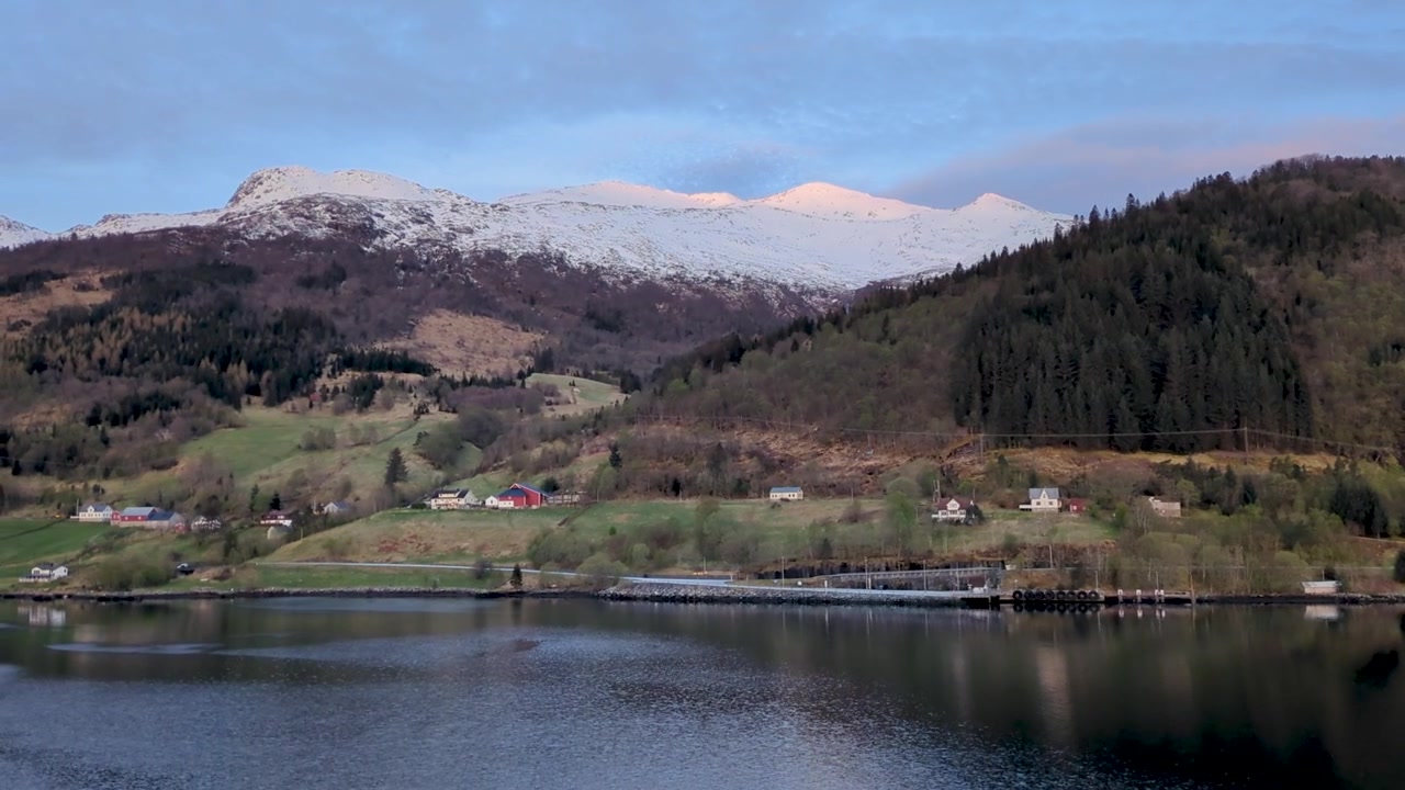 Adembenemend Noors fjord met zonovergoten besneeuwde bergen en dorpskustlijn - Kalm reflecterend water.