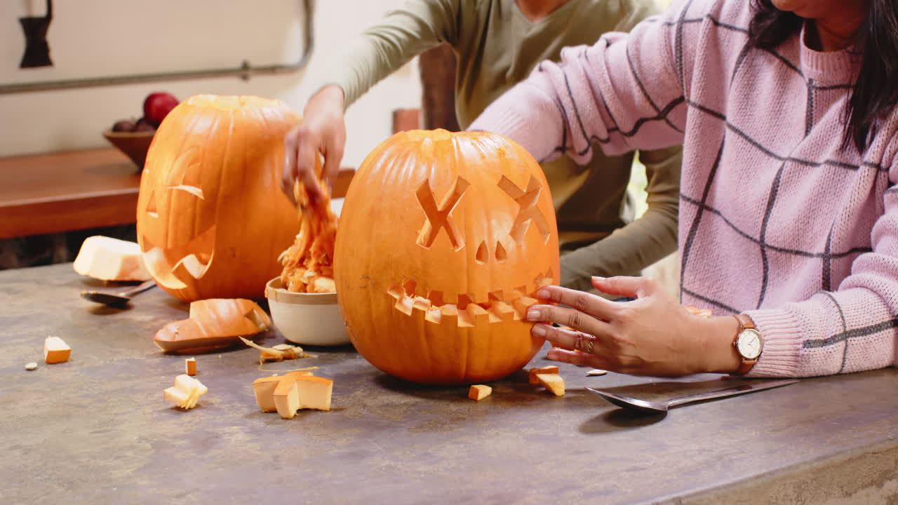 Carving pumpkins together at home, multiracial grandmother and young woman, halloween time