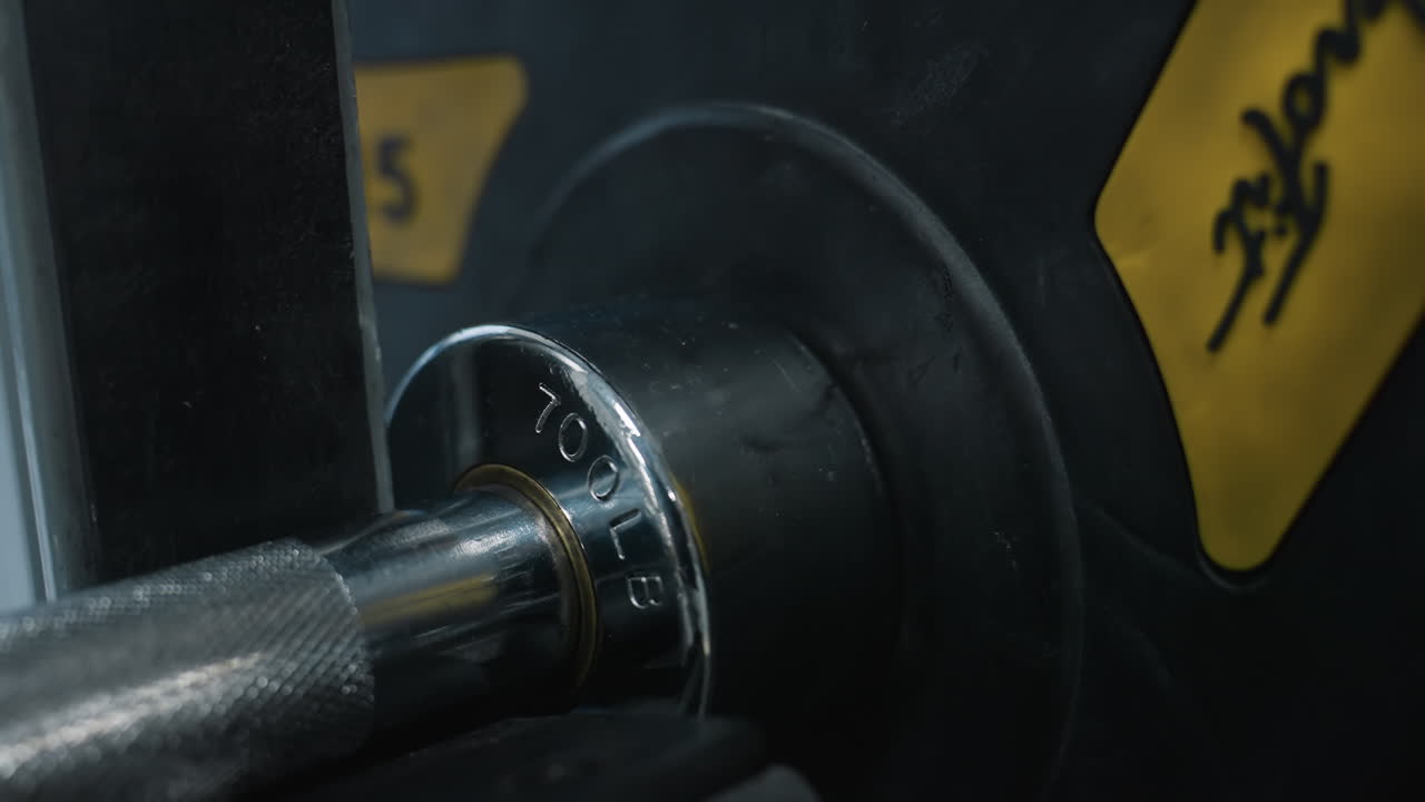 Close up of person inserting metal weight plate onto chrome barbell sleeve on rubber gym flooring, showing hands sliding heavy plate into position during workout setup and equipment preparation