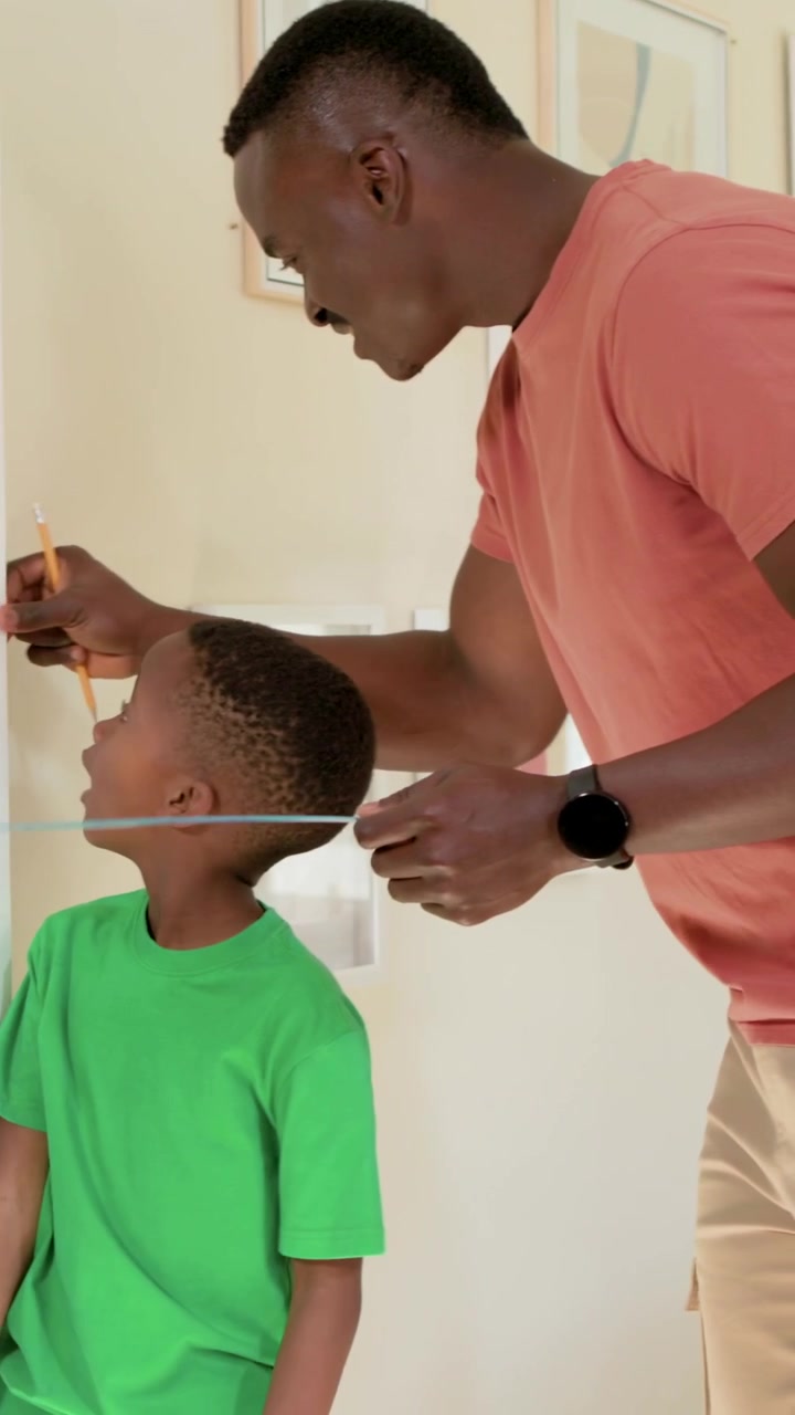 Vertical video: Entering hall dad measuring son against wall to mark height with tape and pencil