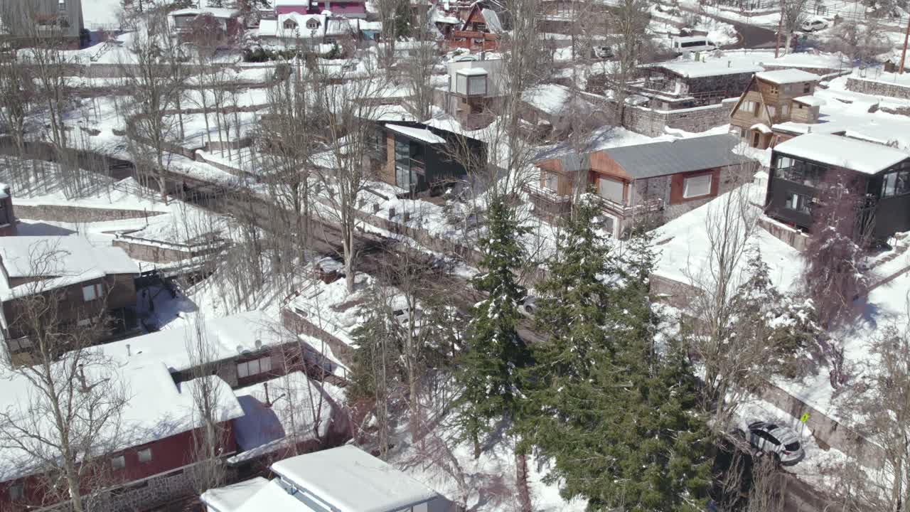 Bird's eye view of native cabins and leafless trees in the snowy mountain village of Farellones, Chile